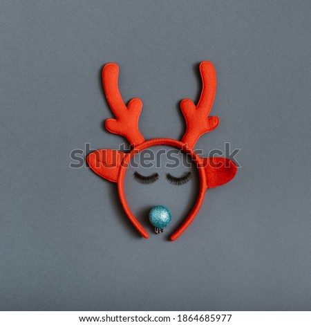 Creative Christmas reindeer idea made of artificial  eyelashes, red bauble decoration and antlers on grey background. Modern winter holidays idea. Flat lay top view composition