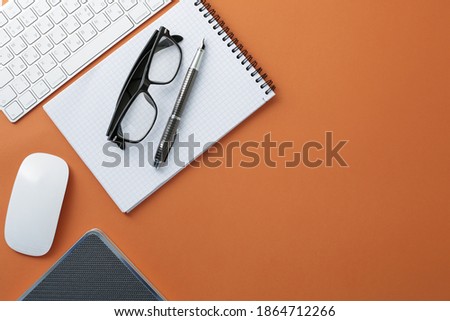 Glasses keyboard mouse pen notepad and diary on orange background