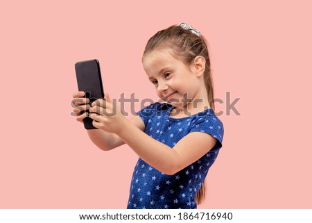 The girl looks at the camera and takes a selfie with a smartphone in her hands. In a blue dress with a small star print. Pink isolated background.