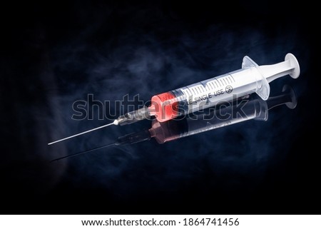 syringe with red liquid for vaccine injection isolated on a black background. decorated smoke or steam. coronavirus vaccine concept. studio shot.