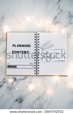 planning content for social media conceptual image, notebook with photo and video icon next to text and progress bar loading surrounded by fairy lights
