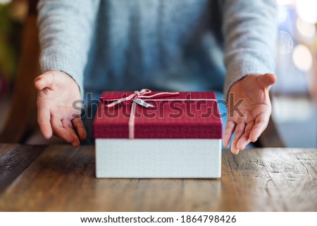 Closeup image of a woman giving and showing a red gift box