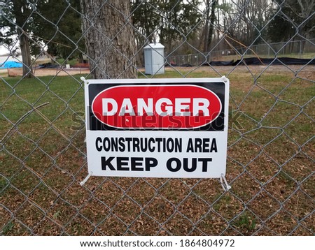 danger construction area keep out sign on fence with outhouse