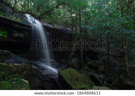 Waterfall landscape. Focus on waterfall, blurred leaves. Beautiful waterfall in tropical rainforest with  rocks and blurred leaves.  Adventure destination in Asia. Slow shutter speed technique.