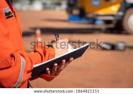 Action of safety officer is taking note on checklist with blurred background of crane truck vehicle. Safety inspection audit in heavy operation concept photo, selective focus at the person's hand. Royalty-Free Stock Photo #1864821151