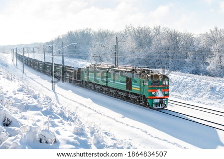 A powerful electric locomotive VL8 pulls a long freight train along snow-covered train tracks. Sunny winter weather. Ukrainian railways Royalty-Free Stock Photo #1864834507