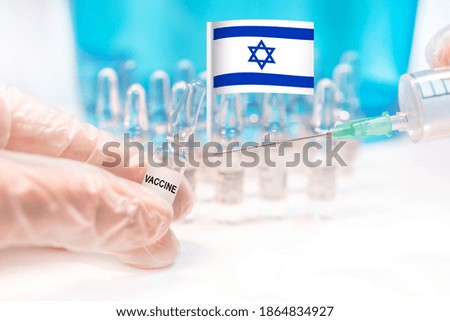 Hands holding a vaccine vial and a syringe with rows of the same capsules and a flag of Israel (State of Israel), illustrating plans for global vaccination against Covid-19 (SARS-CoV-2, coronavirus).
