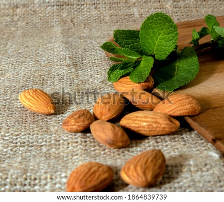Peeled almonds and a small bunch of fresh mint lying on a sack cloth and aged wooden board