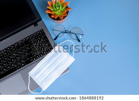 Blue desktop with laptop, glasses, medical mask. The concept of the workplace during the epidemic. Top view with space for your text or app. Flat lay