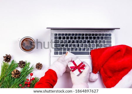 Santa Claus hands in medical latex gloves holding Christmas gifts and laptop on white background with Santa`s hat and vintage gift box. Christmas and New Year holidays present concept.