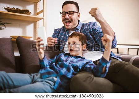 Smiling father and cute little son using phone apps together, watching cartoons or video, playing game.