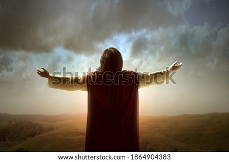 Rear view of Jesus Christ raised hands and praying to god with a sunrise sky background Royalty-Free Stock Photo #1864904383