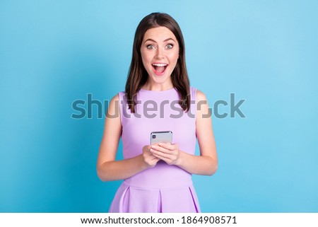 Photo of amazed cheerful young woman hold phone comment reaction isolated on bright blue color background