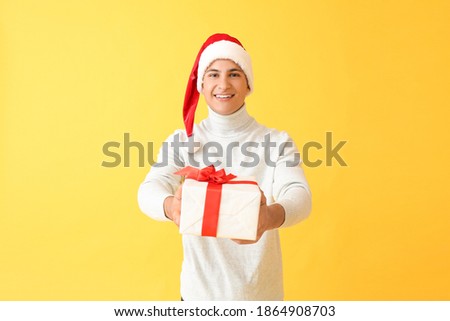 Handsome man in Santa hat and with gift on color background
