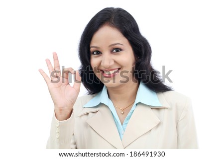 Happy young business woman making Ok gesture against white