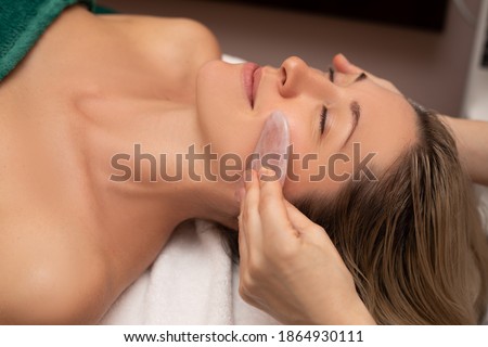 Young and beautiful woman during Chinese traditional massage - Gua Sha. Close-up photo. Beauty treatment in SPA salon. Beauty tools in the hand of beautican