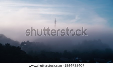 Early morning sunrise with thicker fog or mists over a 5G comm tower, image with slight movie grain Royalty-Free Stock Photo #1864935409