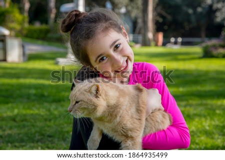 Gymnastics girl holding a ginger cat on her arms in the park