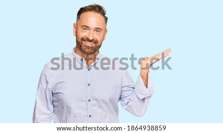 Handsome middle age man wearing business shirt smiling cheerful presenting and pointing with palm of hand looking at the camera. 