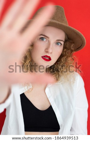 Young woman with green eyes wearing hat over red background. Girl showing stop gesture. Women's rights concept
