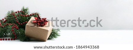 Christmas gift on the pine tree branch with a red bow and red garland background