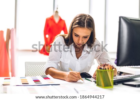 Portrait of young beautiful pretty woman fashion designer stylish sitting and working.Attractive young girl use desktop conputer and colorful fabrics at fashion design studio