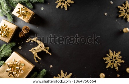 Christmas and new year background concept. Top view of Christmas gift box, spruce branches, pine cones, reindeer, christmas ball and snowflake on black wooden background.