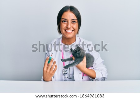 Young hispanic veterinary girl smiling happy putting vaccine on cat working at the clinic