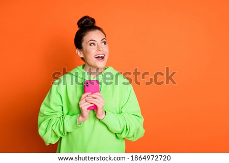 Photo of charming woman wear green hoodie holding modern gadget looking empty space isolated vivid orange color background