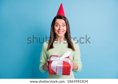 Photo portrait of excited girl holding red present wearing cone isolated on pastel blue colored background