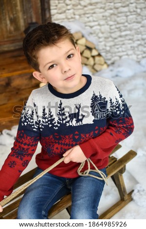 Portrait of boy on sled in front of old rustic door. Christmas decoration. Happy child in front of rustic cottage wait a New Year