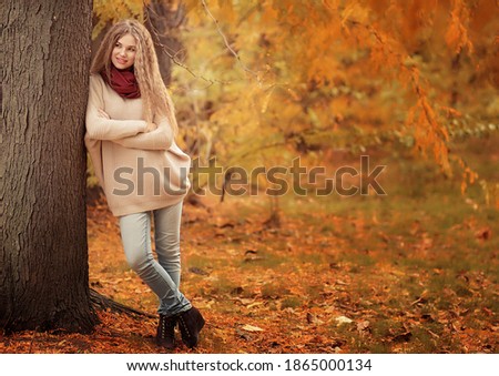 A beautiful girl stands near a tree in the autumn forest. Image with selective focus and toning. Image with noise effects. Focus on the eyes.