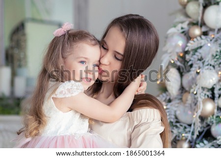 gentle mother kissing, congratulating her daughter on Christmas.  girl smiling, hugging woman on xmas. happy family at home for new year.