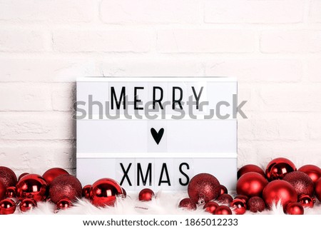 Merry Xmas text on white Lightbox with red balls on white fur against white brick wall.