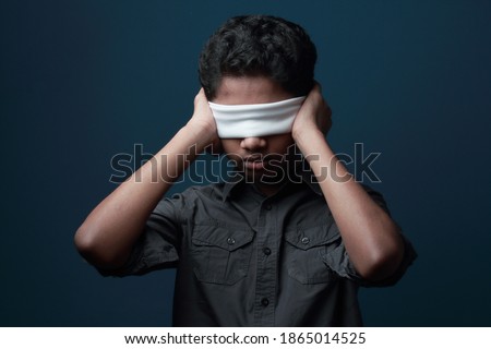 Light and shade portrait of a blindfolded  boy in a dark background closing his ears with hands