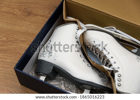 Opened box with new white figure skates for women. The box lies on a light brown wooden background. Selective focus.