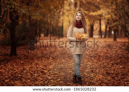 A beautiful girl walks through the autumn forest. She has yellow leaves in her hands. Image with selective focus and toning. Image with noise effects. Focus on the eyes.

