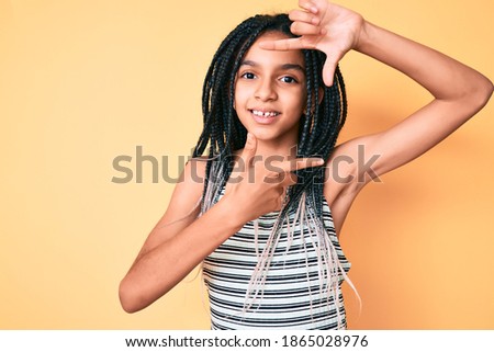 Young african american girl child with braids over yellow background smiling making frame with hands and fingers with happy face. creativity and photography concept. 