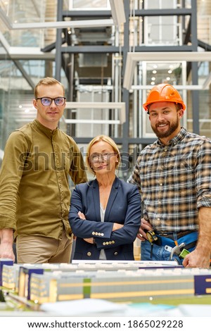 team of architect and engineer led by female director, adult blonde woman stand in the center between two confident men, they look at camera smiling Royalty-Free Stock Photo #1865029228