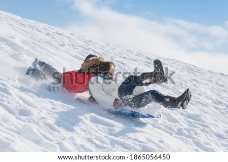 Asian child falls off a sled while playing with his mother.