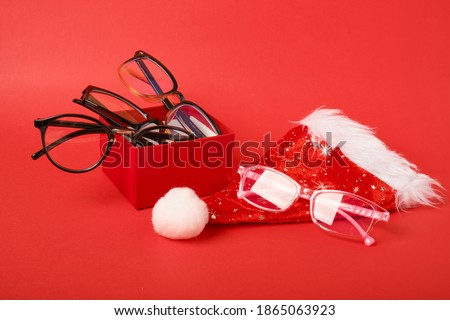 red gift box, various glasses for vision and santa claus festive christmas hat on red background