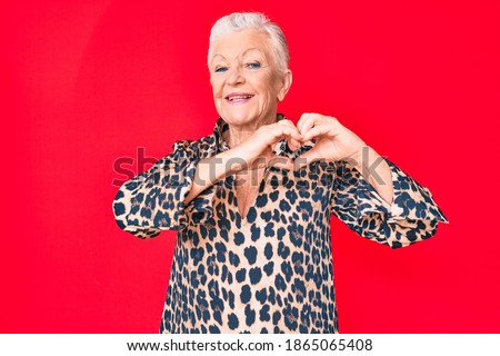 Senior beautiful woman with blue eyes and grey hair wearing casual and modern leopard animal print shirt smiling in love showing heart symbol and shape with hands. romantic concept. 