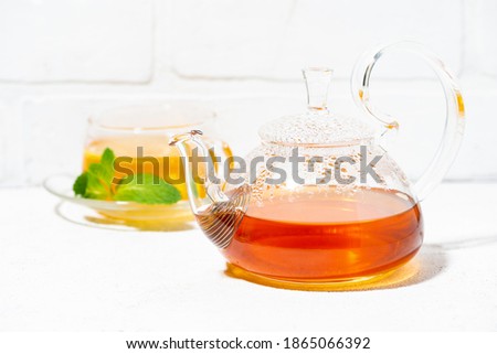 glass teapot of tea with lemon, ginger and mint to enhance immunity on white background, closeup