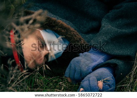 Poor dirty man lies dead on the ground A homeless man in a medical mask lies on the wet ground unconscious close-up