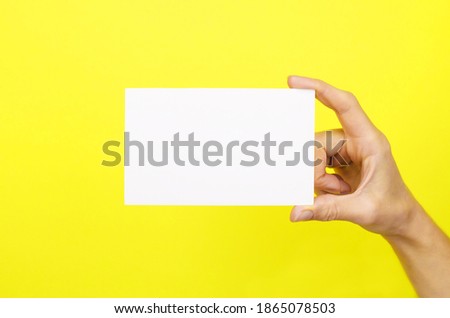 White card in a female hand on a yellow background