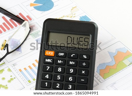 Calculator with text on the display Dues it is on the financial charts with eyeglasses, can be use as financial and business concept