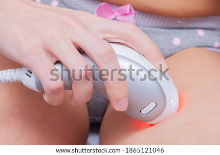 Woman using an intense pulsed light epilator to remove unwanted hair from her bikini area and legs. Spa procedure at home, concept