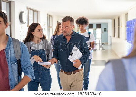 High school student asking doubt to professor. Mature man professor answering to girl in university campus. High school lecturer talking to schoolgirl at the end of the lesson while walking in hallway Royalty-Free Stock Photo #1865153410