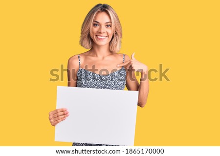 Beautiful caucasian woman holding blank empty banner pointing finger to one self smiling happy and proud 