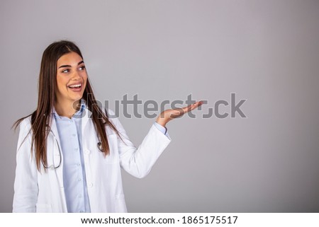 Doctor with stethoscope over neck looking at camera isolated on gray. Beautiful smiling woman doctor portrait in studio she is confident mood, she is pointing the right side, isolated studio shot